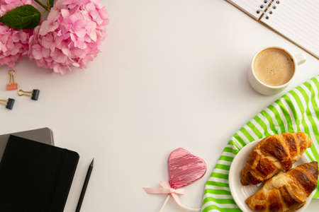 Table top of work space frame with cup of coffee, croissants, pink hydrangea and notebooks.の写真素材