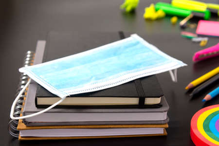 Face mask, colorful pencils, rainbow eraser, notebook, sticky notes. Flat lay. Abstract educational background.の写真素材