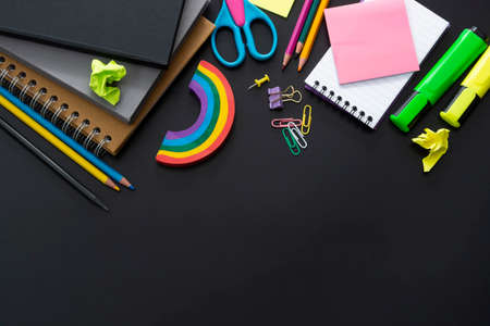 Back to school concept. Colorful pencils, rainbow eraser, notebook, sticky notes and office supplies on black background. Copy space.の写真素材