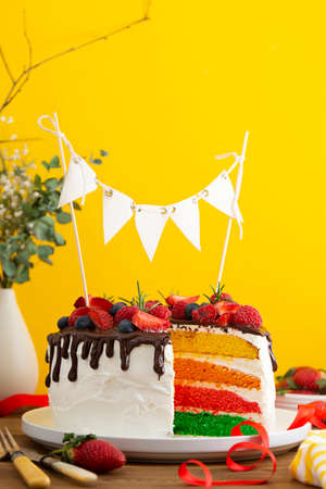 Rainbow whole cake with fresh berries on yellow background.の写真素材
