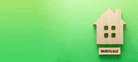 Mortgage banner word and wooden house. Home insurance. Rent, buy house. Green background with copy space.の写真素材