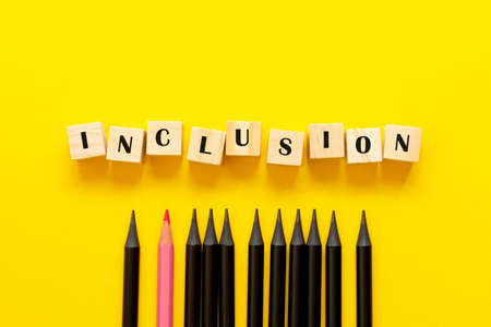 Inclusion concept word on wooden cubes and pencils on yellow background