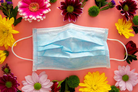 Medical blue face protective mask with colorful flowers on pink background. Creative concept of seasonal allergies. Spring 2021 concept.の写真素材
