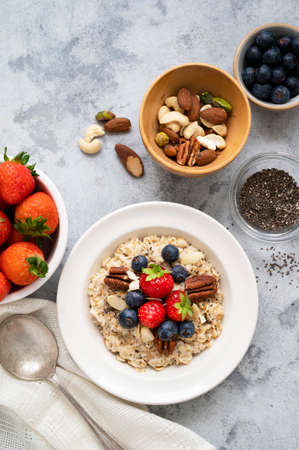 Oatmeal porridge with fresh berries blueberry and strawberries in white bowl over grey background