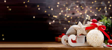Christmas winter baner. White sleigh, shiny star, red bauble, gift boxes, fir branches and candy cane. Rustic wooden background.の写真素材