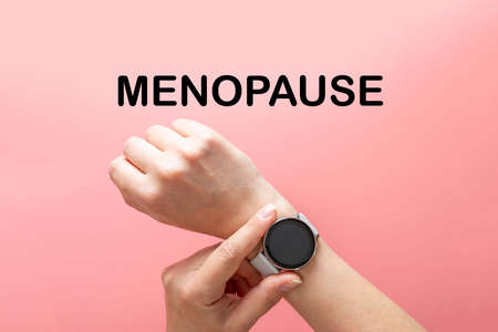Menopause word text, hands with watch, abstract concept of time, pink background, top viewの写真素材