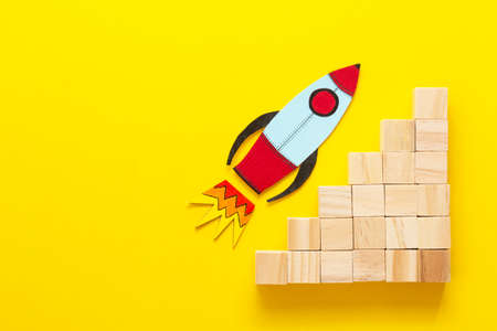 Business growth concept abstract yellow background. Colorful rocket, paper cut wooden blocksの写真素材