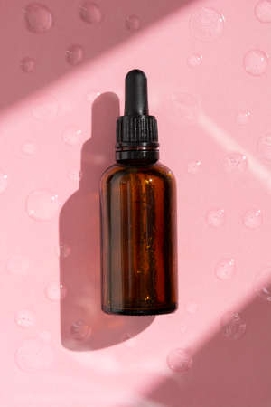 Essence serum. Dark pipette botle, cosmetics skin care. Pink background.