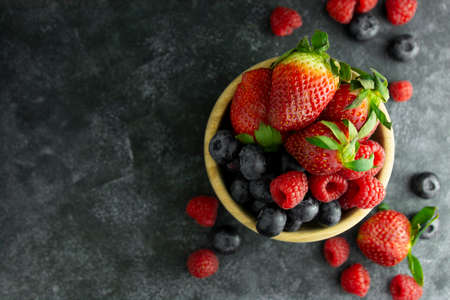 Assortment berries blueberries, strawberries and raspberries in wooden bowl. Dark mood background.の写真素材