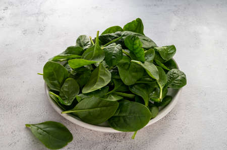 Fresh spinach leaves in a bowl on gray background. Healthy food ingredientsの写真素材