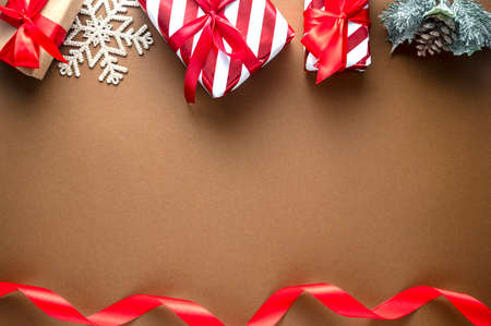 Christmas gift boxes wrapped in craft paper with red bow and winter decorations on brown background....