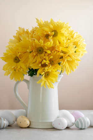 Yellow chrysanthemum flower bouquet in vase and easter eggs on the table. Abstract easter spring backgroundの写真素材