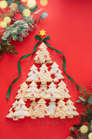 Christmas tree made from christmas tree shaped cookies on red background, with winter decorations and bokeh lightsの写真素材