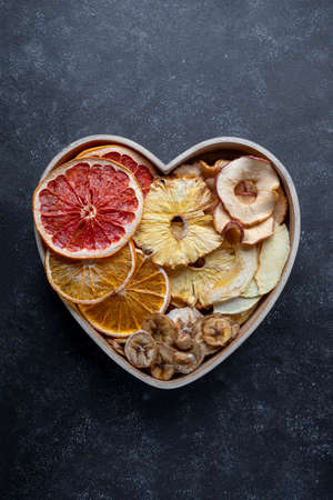 Dried fruit slices in heart shaped bowl. Dried orange, grapefruit, pineapples, banana.の写真素材