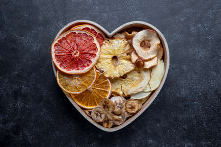 Dried fruit slices in heart shaped bowl. Dried orange, grapefruit, pineapples. Healthy snack or dessertsの写真素材
