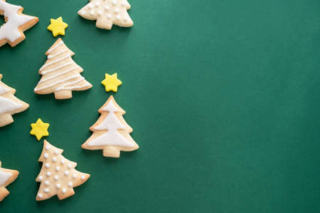 Christmas tree cookies with icing and stars. Festive winter pastry, home baking concept, green background top view, copy spaceの写真素材