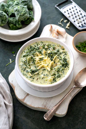 Creamed spinach with garlic and cheese in a white bowl on dark background