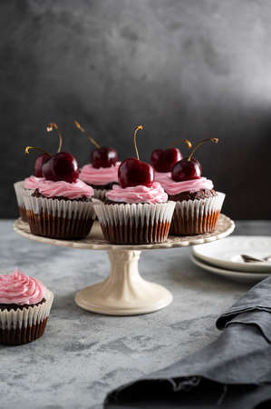 Chocolate cupcakes with fresh cherries and pink cream on cake stand. Beautiful dessert. Dark...
