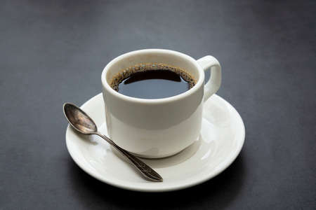Coffee drink. White cup of coffee top view, spoon and plate on dark backgroundの写真素材