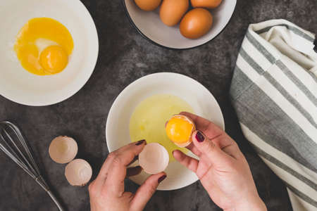 Woman's hands breaking an fresh egg. Dark background. Food flat lay. Menu, cooking pastry concept.
