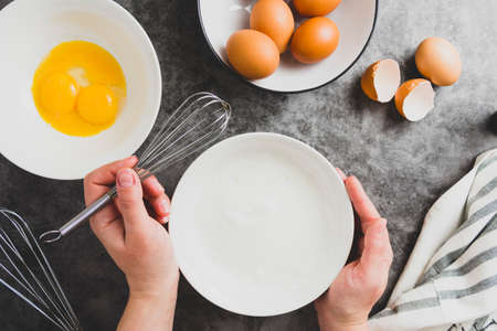 Whipping white eggs with whisk, in a bowl. Top view of woman's hands mixing eggs.の写真素材