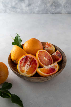 Oranges in wooden bowl, on bright background, whole and slices with leaves fresh citrus fruitの写真素材