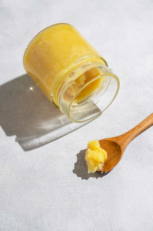 Ghee in a glass jar made with sunflower oil on a light background, copy space. Hard light.の写真素材