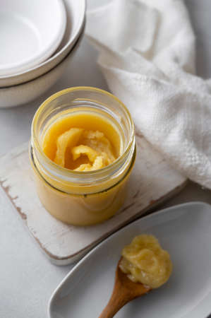 Ghee in a glass jar made with sunflower oil on a light background, copy space. Hard light.