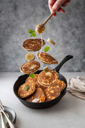 Levitating pancakes in frying, skillet pan with honey,banana, butter and mint leaves, breakfast foodの写真素材