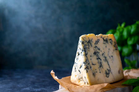 Blue cheese mold cheese slice on cutting board with basil leaves, lifestyle food