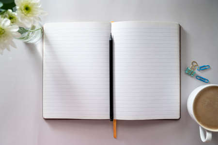Open notebook, empty pages with cup of coffee, table top. Spring flowers.