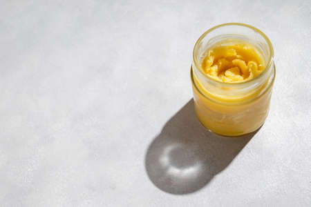 Ghee in a glass jar made with sunflower oil on a light background, copy space. Hard light.の写真素材