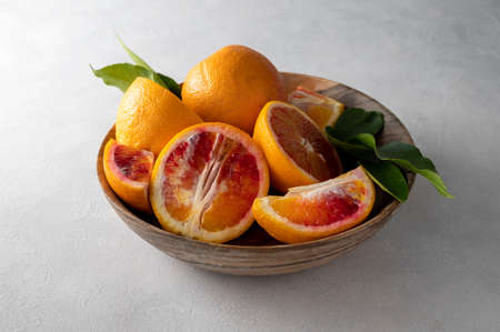 Blood oranges in wooden bowl, on bright background, whole and slices with leaves fresh citrus fruitの写真素材