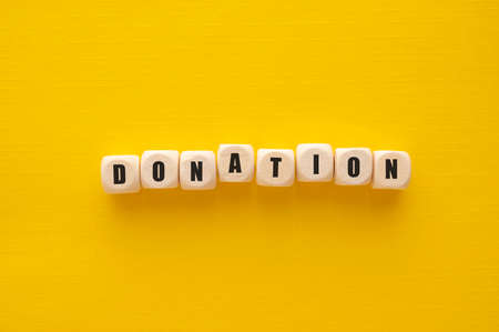 Donation word over wooden blocks, yellow background. Charity kindness concept