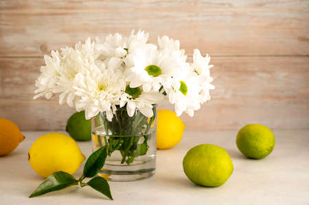 Bouquet of white chrysanthemums in glass with whole lemons and limes. Abstract floral and fruits rustic backgroundの写真素材