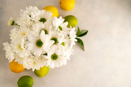 Bouquet of white flowers in glass with whole lemons and limes. Abstract floral and fruits rustic backgroundの写真素材