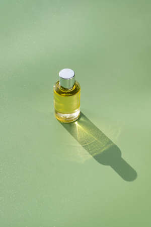 Transparent bottle of perfume or aroma oil essence on a green background. Natural light and shadowsの写真素材