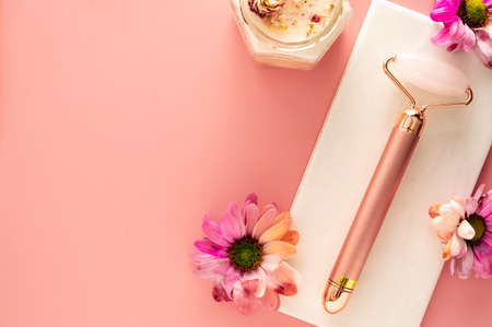 Self care concept. Pink quartz face roller with aroma candle and flower on pink background. Minimal beautyの写真素材
