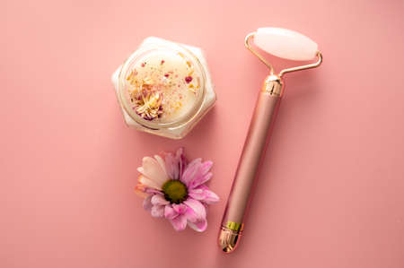 Pink quartz face roller with aroma candle and flower on pink background. Minimal self care concept, top viewの写真素材