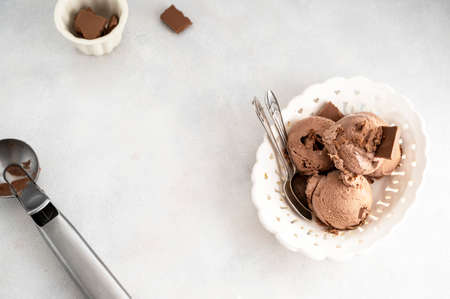 Three brown chocolate ice cream balls, scoops in white bowl over gray background, copy space