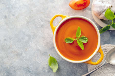 Tomato soup with fresh basil in orange bowl. Bright background. Healthy food concept.の写真素材