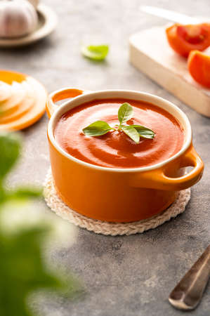 Tomato soup with fresh basil in orange bowl. Bright background. Healthy food concept.の写真素材
