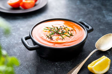 Tomato soup with fresh herbs in black bowl. Dark background. Vegan creamy soupの写真素材