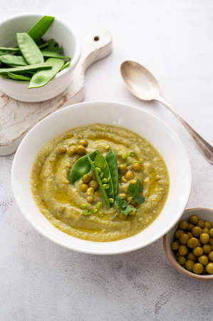 Green cream soup with green fresh peas on bright background. Healthy, vegan foods