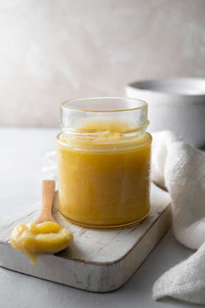 Ghee in a glass jar made with sunflower oil on a light background, copy space. Hard light.