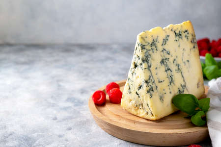 Blue cheese, dor blue or roquefort mold cheese slice on cutting board with basil leaves and...