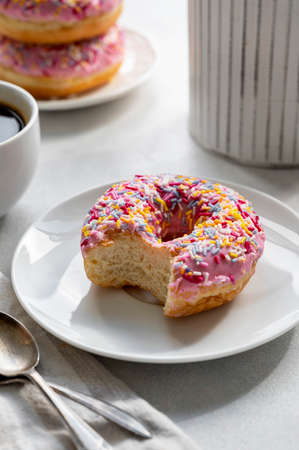 Pink donut with sprinkles and coffee cup for breakfast, bright background