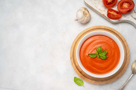 Tomato soup with fresh basil in orange bowl. Bright background. Healthy food concept.の写真素材