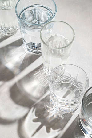 Glasses of water and sharp shadows stands on a bright background. Drinking water concepts