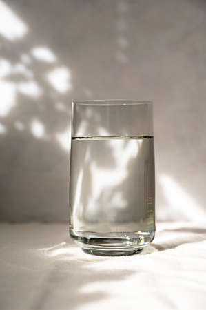 Glass with water, abstract summer shadows on background